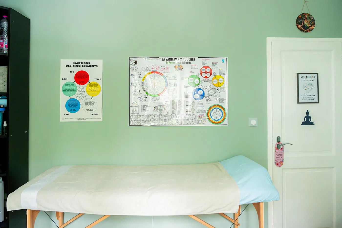 Salle de soin du cabinet à Sillingy : table de massage, murs vert sauge et planches de kinésiologie au mur