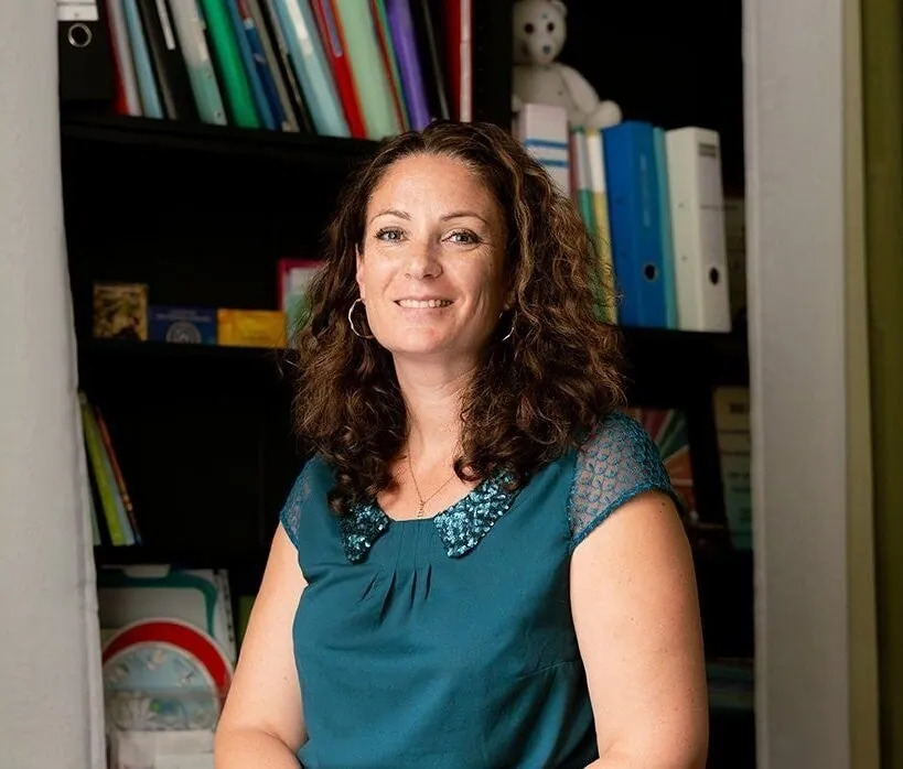 Portrait d'Émilie Ravoire, kinésiologue, souriante devant la bibliothèque de son cabinet