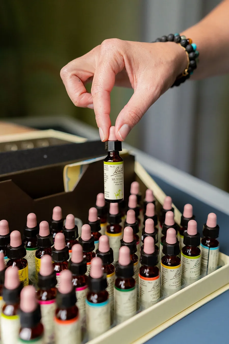 Main qui prend un flacon de fleurs de Bach dans un coffret de flacons en verre ambré